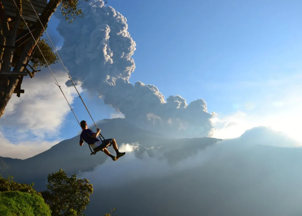 Volcán Tungurahua erupts as a man swings on the Casa del Arbol in the foreground in Ecuador. Wheely Tyred Best multi-day tours in Baños