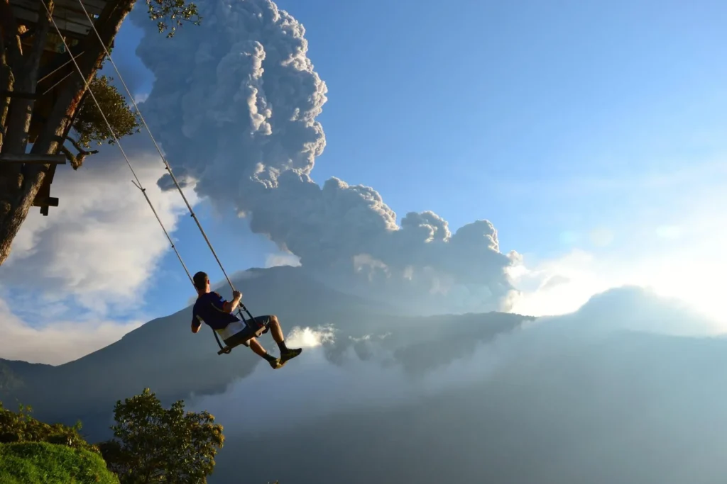 Volcán Tungurahua erupts as a man swings on the Casa del Arbol in the foreground in Baños, Ecuador. Wheely Tyred best Cotopaxi multi-day tours