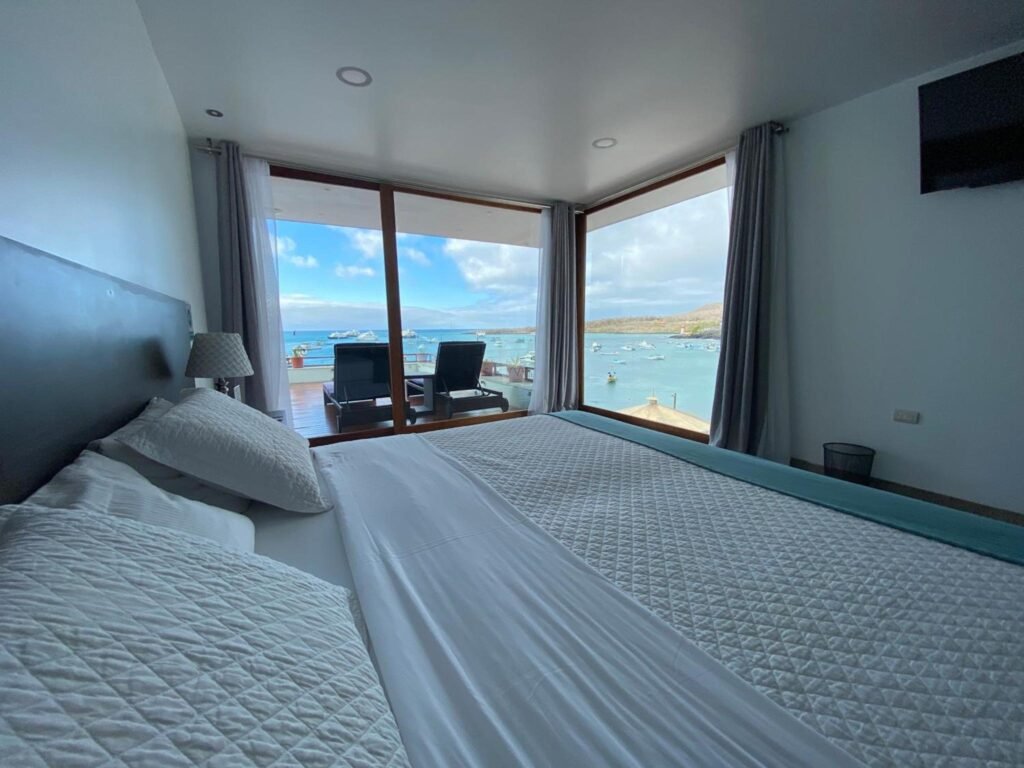 A bedroom in the Galapagos Sunset Hotel with boats seen through the window, in Puerto Baquerizo Moreno, San Cristobal, Ecuador