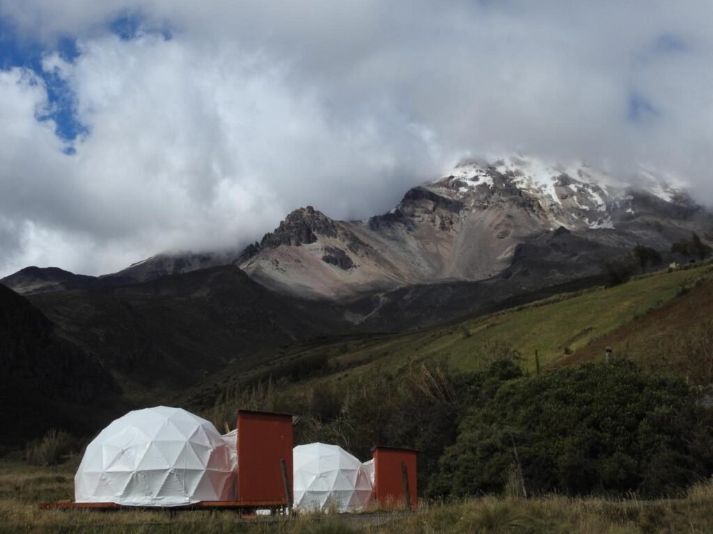 Two white dome tents sit on a plain under Chimborazo, Ecuador