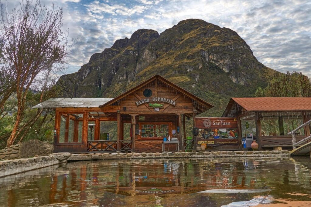 The fishing pool of Estancia San Juan sits in front of wooden buildings. A huge rocky outcrop is behind, near Cajas National Park and Cuenca, Ecuador