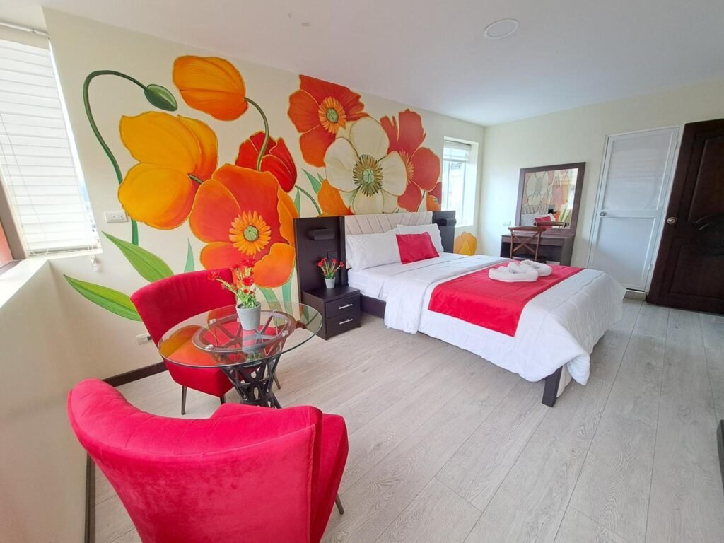 A room at the Hotel Loja Bella with flowers painted behind a double bed, in Ecuador