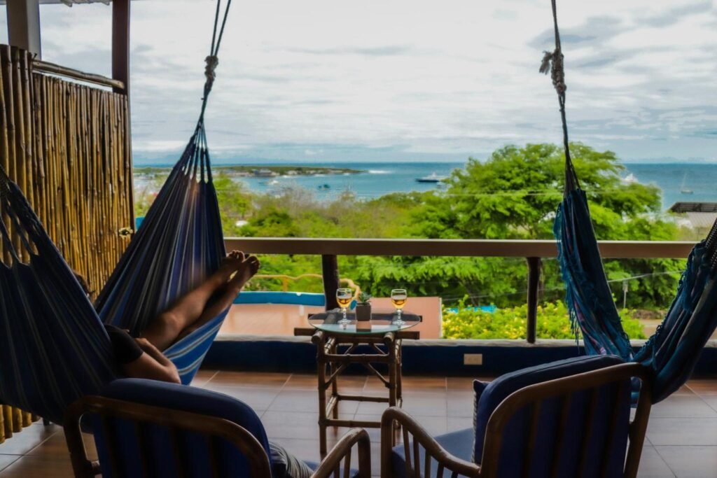A woman lies in a hammock with the beach and on sea in the distance on the balcony of Casa Playa Mann in Puerto Baquerizo Moreno, San Cristobal, Galapagos, Ecuador