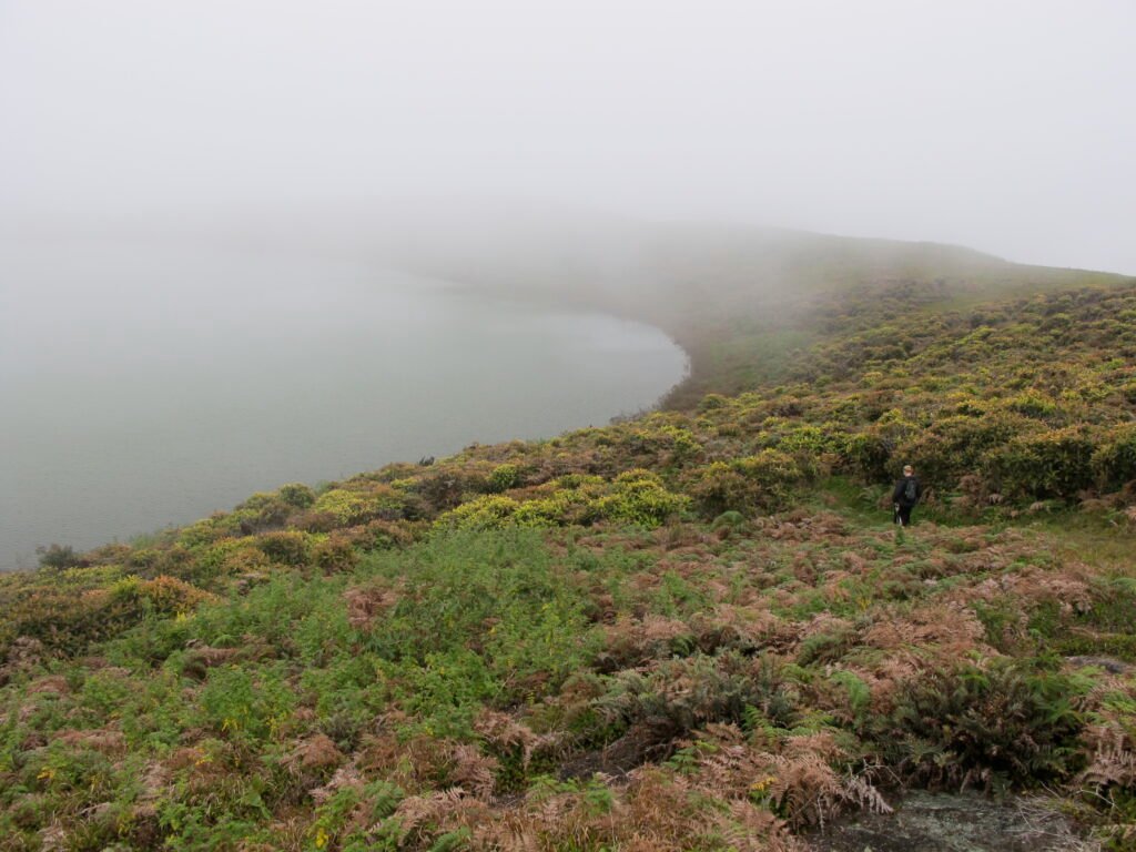 A man walks towards Laguna El Junco, covered in clouds, on San Cristobal, Galapagos, Ecuador