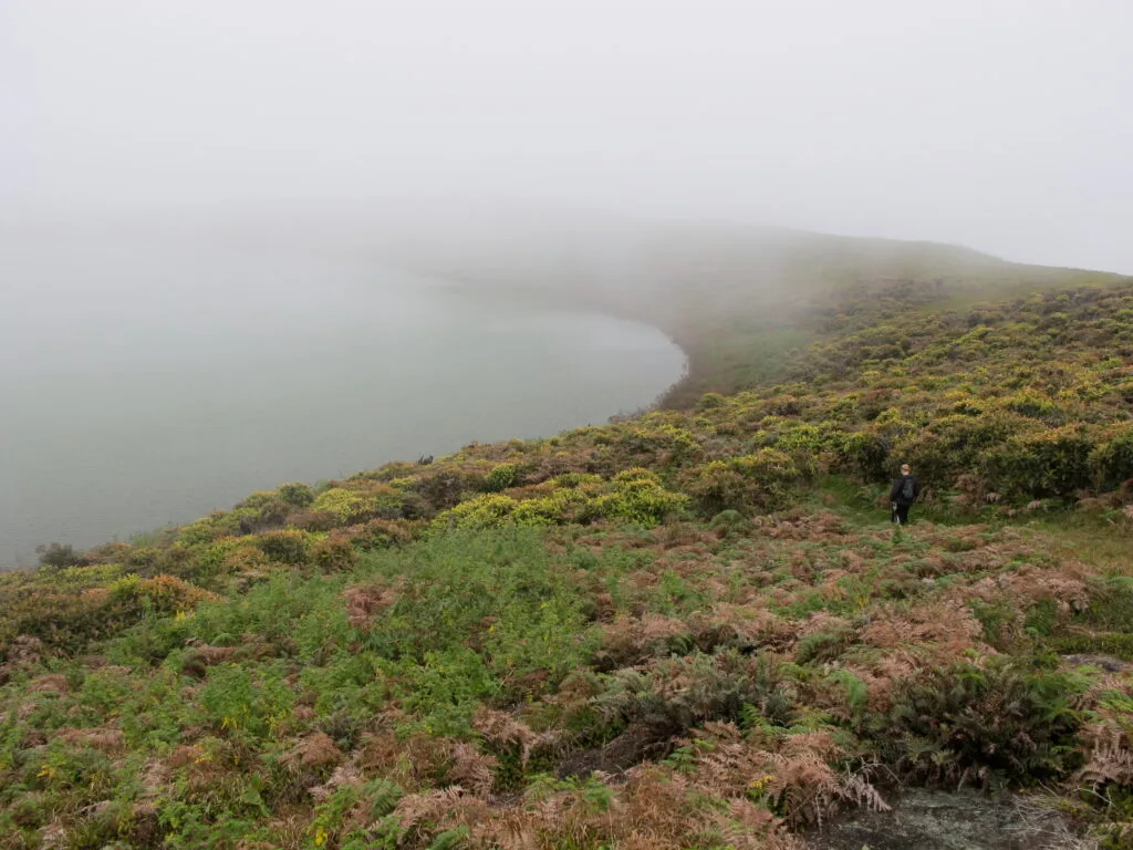 A man walks towards Laguna El Junco, covered in clouds, on San Cristobal, Galapagos, Ecuador