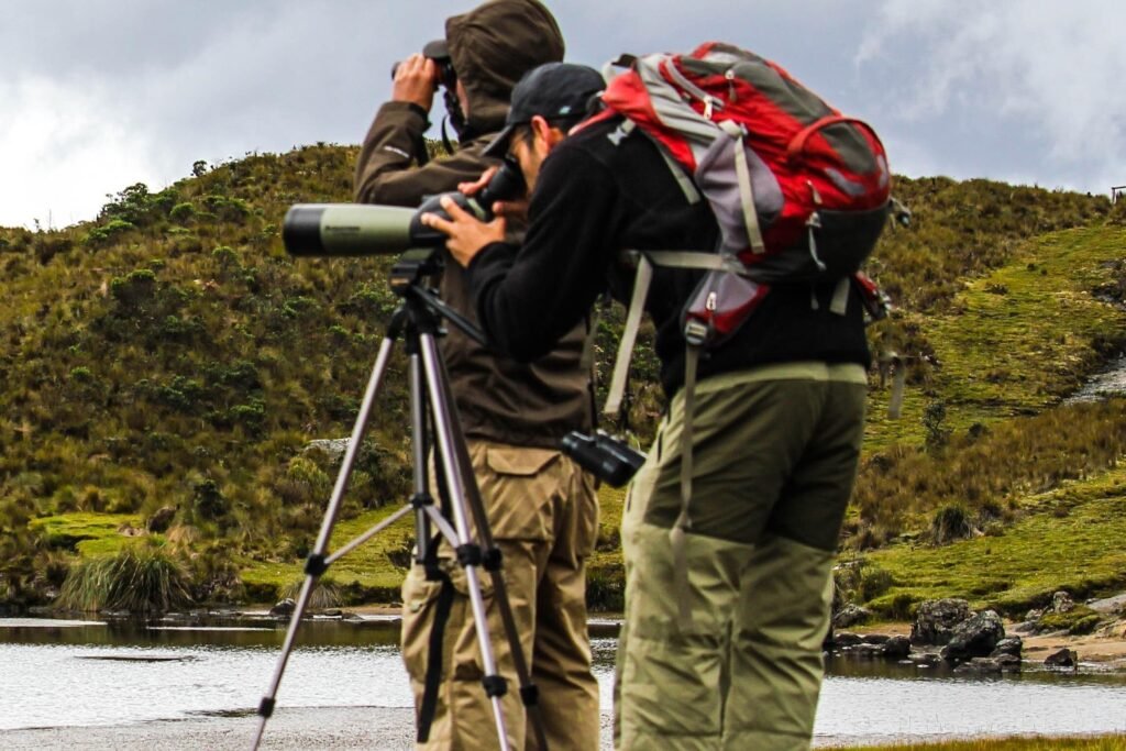 Two birdwatchers in outdoor gear look through telescopes beside a lake in Cajas National Park, Cuenca, Ecuador