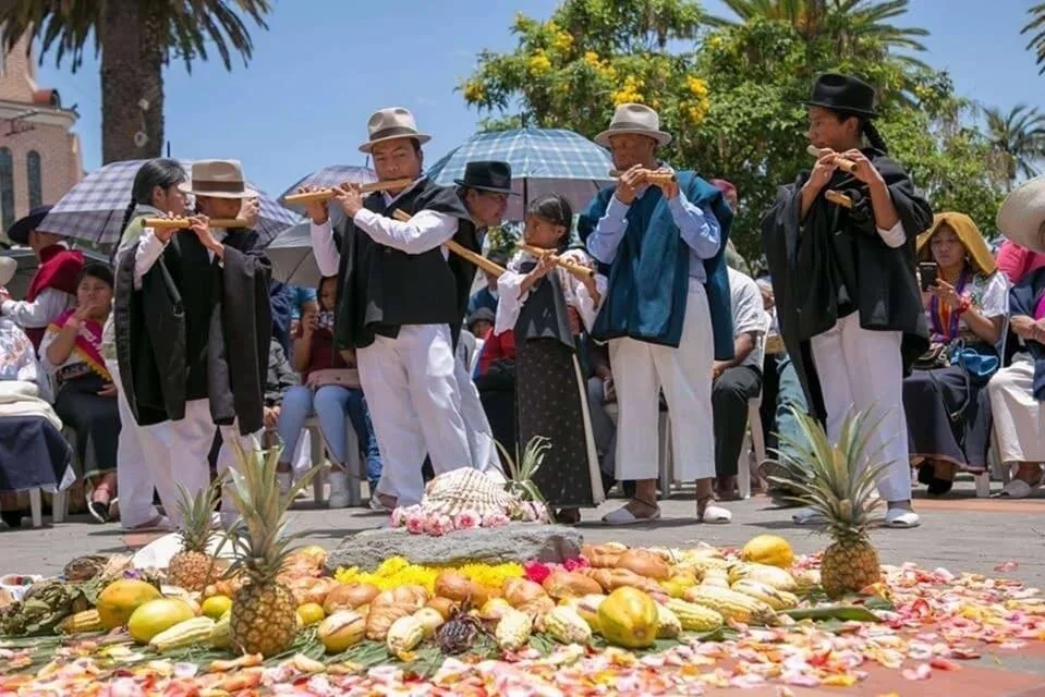 A group of indigenous musicians play pipes in front of some flowers in Otavalo, Ecuador
