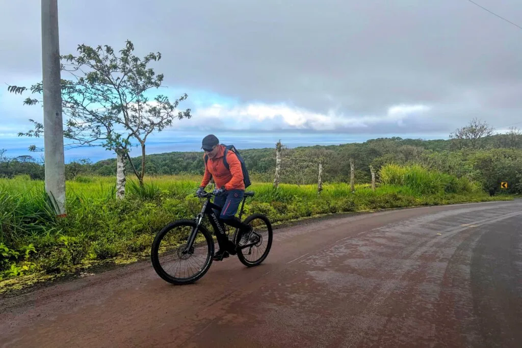 A man climbs a hill while standing on an red Specialized e bike on San Cristobal, Galapagos, Ecuador