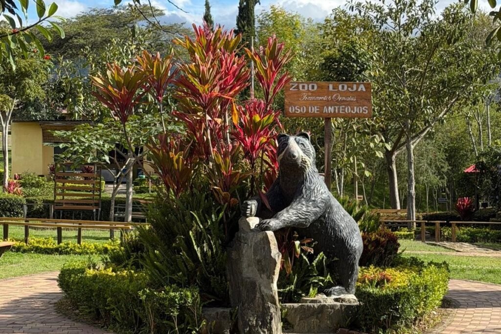A statue of a bear beside a large plant at the entrance to Loja Zoo, Ecuador