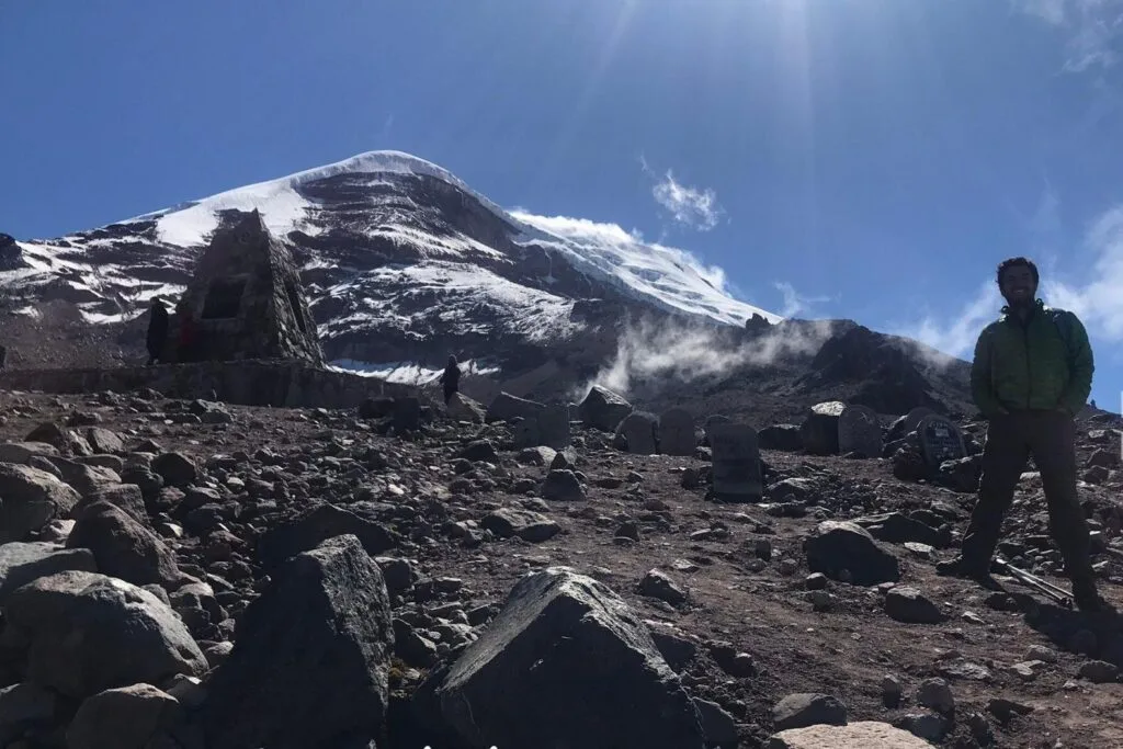 A man in a green jacket stands in front of a refuge on a sunny day on Chimborazo, Ecuador