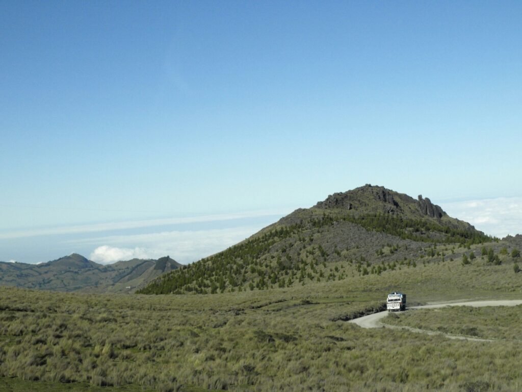 A chiva bus drives across a dirt track under some hills near Salinas, Guaranda, Ecuador