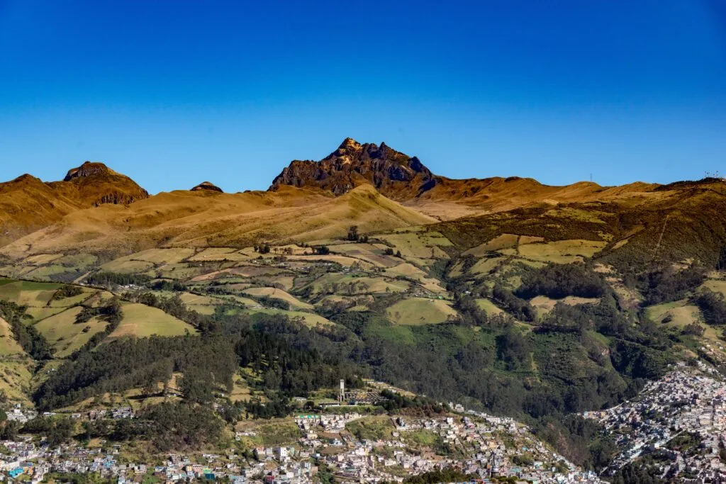 Panoramic view of the Pichincha Mountains and Quito's outskirts, showcasing lush green landscapes under clear blue skies