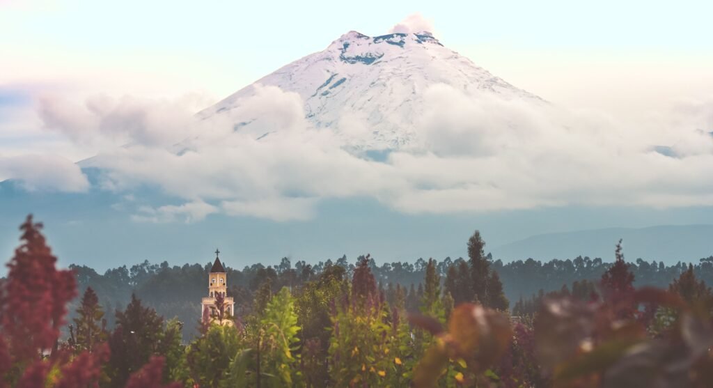 Cotopaxi Volcano towers over a forest with a small church in Ecuador