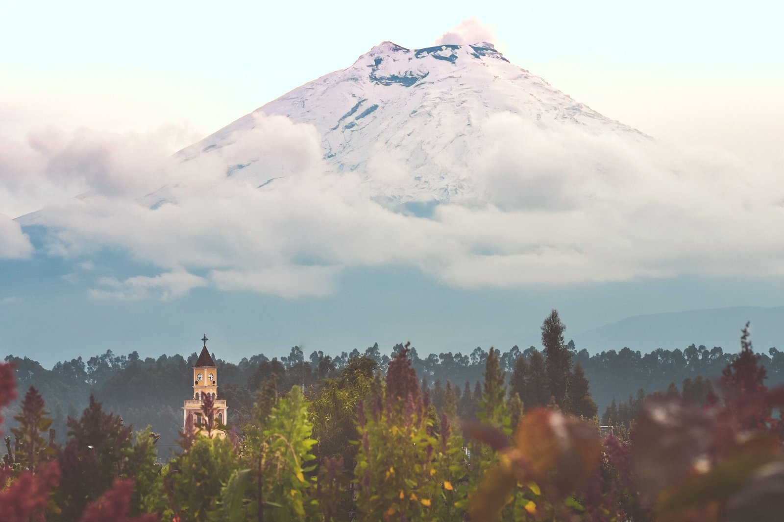 Cotopaxi Volcano towers over a forest with a small church in Ecuador