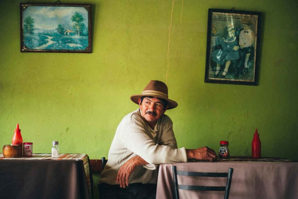An indigenous man in a hat sits in a restaurant surrounded by faded pictures near Ingapirca, Ecuador